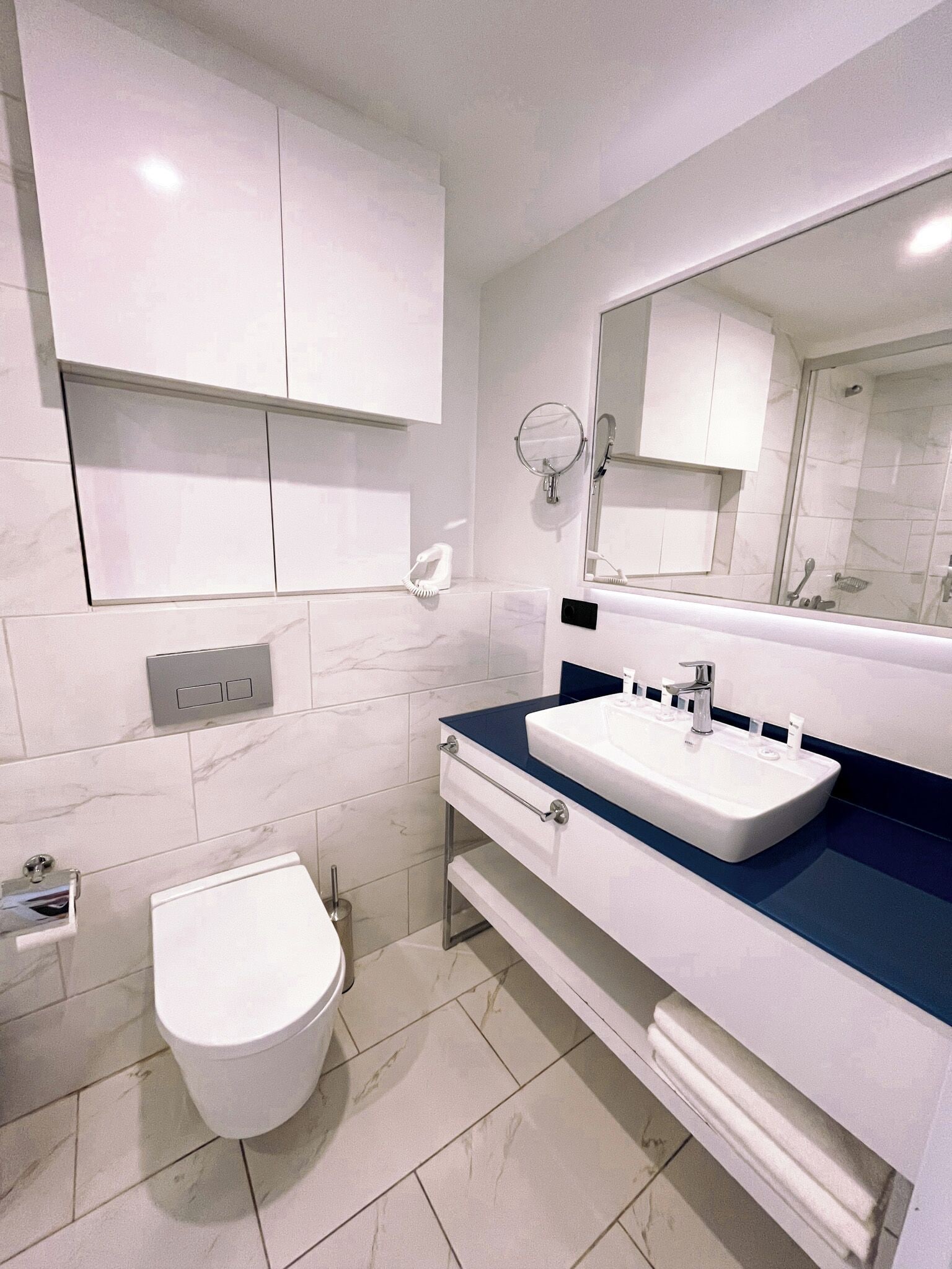 A modern bathroom with a white toilet, a sink with a blue countertop, and a mirror above the sink.