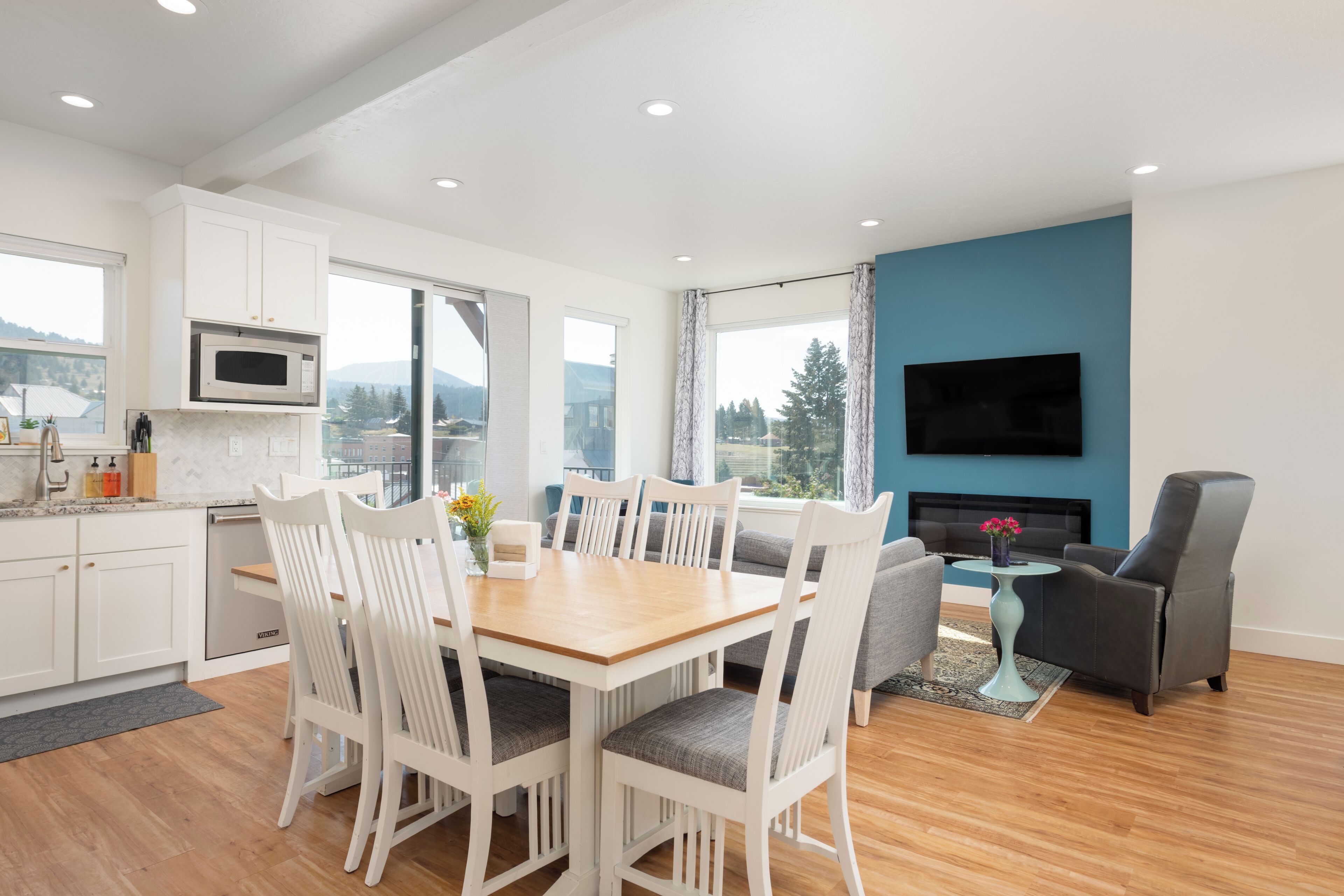 Una cocina moderna con armarios blancos, un microondas y una zona de comedor con una mesa de madera y sillas blancas.