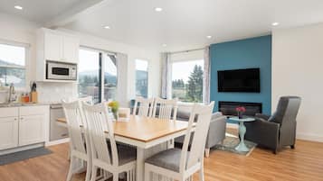 Una cocina moderna con armarios blancos, un microondas y una zona de comedor con una mesa de madera y sillas blancas.