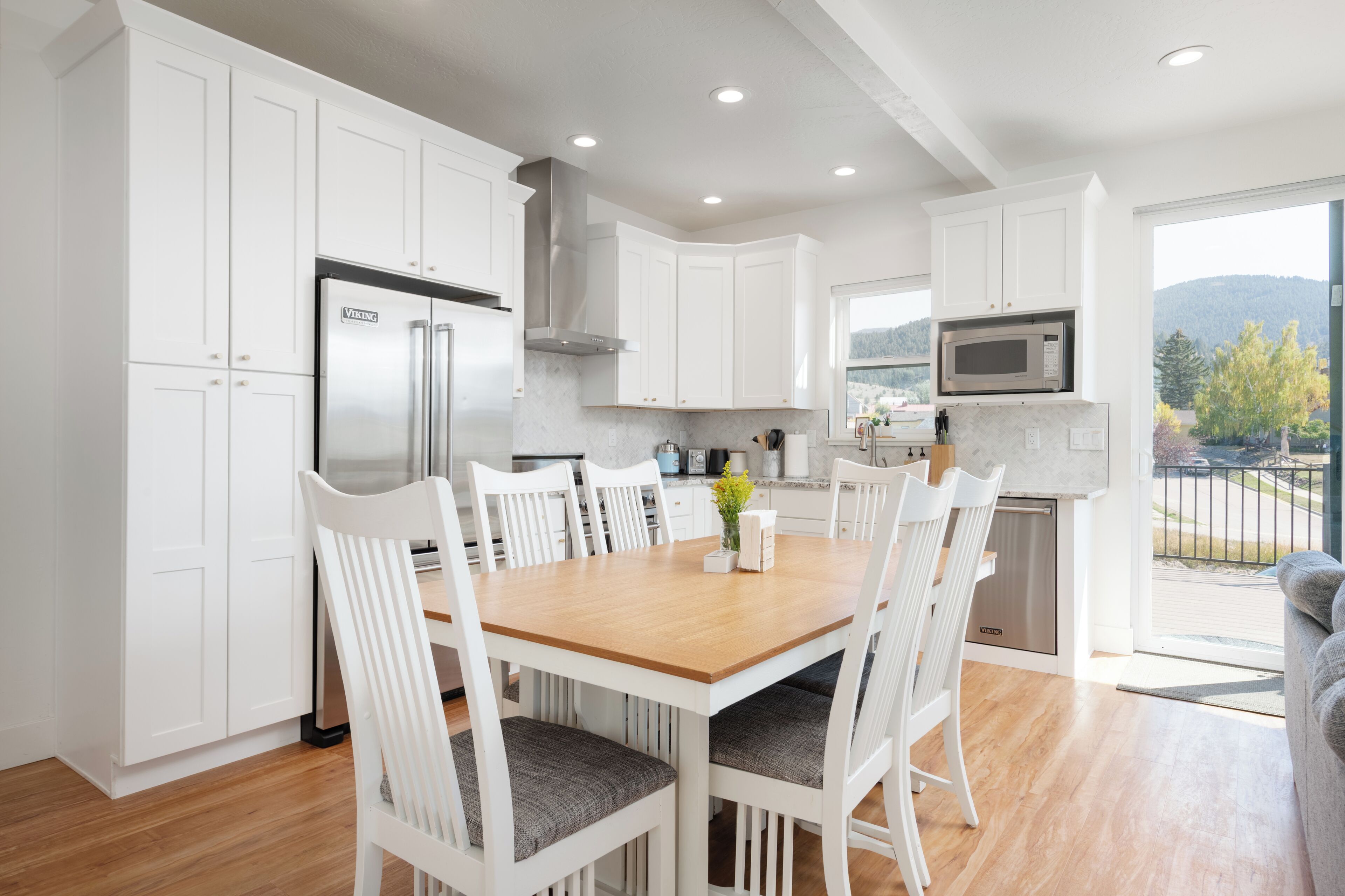 Una cocina moderna con armarios blancos, una mesa de comedor de madera y vistas al exterior.