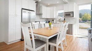 A modern kitchen with white cabinetry, a wooden dining table, and a view of the outdoors.