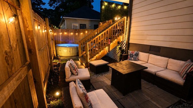 A wooden deck with outdoor seating, a hot tub, and a staircase leading to a covered area. - Walk to Stadium | Hot Tub • Fire Pit • Parking (Atlanta)