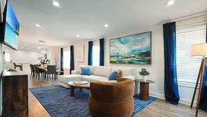 A modern living room with a sofa, armchair, coffee table, and a TV. - Walk to Stadium | Hot Tub • Fire Pit • Parking (Atlanta)