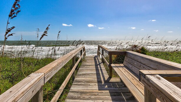 A wooden boardwalk leading to a bench overlooking a beach with waves and grasses. - Legasea - Ocean Front home with direct Beach Access, Large Decks, great for larg (Carolina Beach)