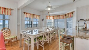 A dining area with a large table and chairs, a ceiling fan, and windows with striped curtains. - Legasea - Ocean Front home with direct Beach Access, Large Decks, great for larg (Carolina Beach)