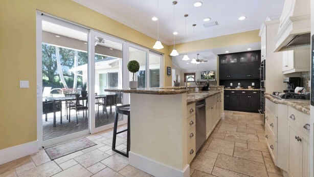 A kitchen with a central island, dark cabinets, and a sliding glass door leading to an outdoor area. - Palm House GolfCourseViews Pool 5bd/5bth&Game Room (Naples)