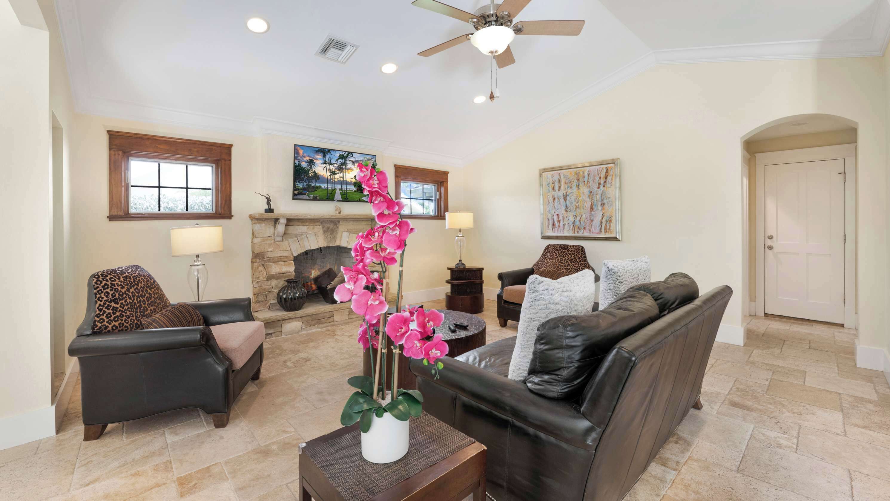 A spacious living room with a stone fireplace, leather sofas, and a ceiling fan.