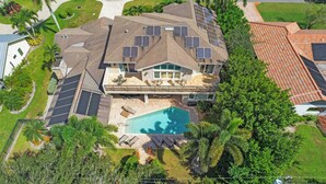 A residential property with a swimming pool, solar panels, and a fenced backyard. - Palm House GolfCourseViews Pool 5bd/5bth&Game Room (Naples)