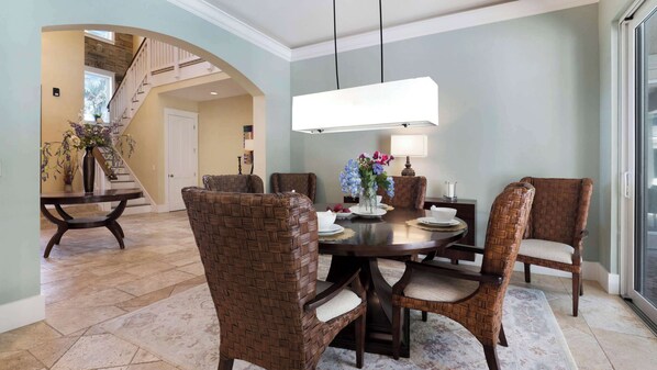 A dining area with a round table, wicker chairs, and a hanging light fixture.