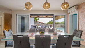 A modern dining area with a glass table, grey upholstered chairs, and a view of an outdoor patio with a pool.