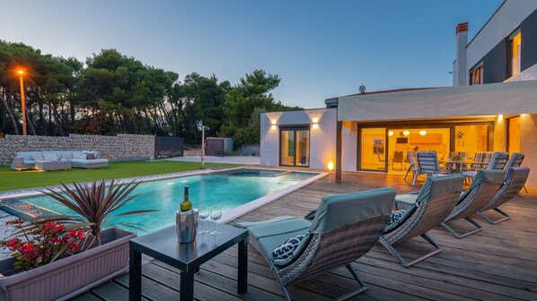 A modern outdoor pool area with lounge chairs, a table with drinks, and a stone wall.