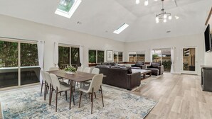 A spacious living area with a dining table, sofas, and a large window offering a view of greenery. - Pet Friendly Sea Pines Retreat (Hilton Head Island)