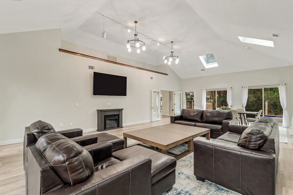 A spacious living room with leather sofas, a wooden coffee table, a flat-screen TV, and a fireplace.