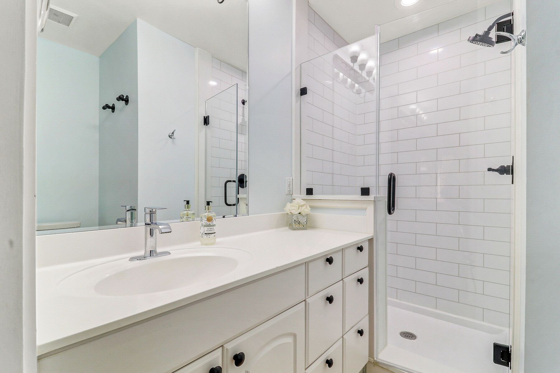 A modern bathroom with a large mirror, two sinks, a shower, and a toilet.