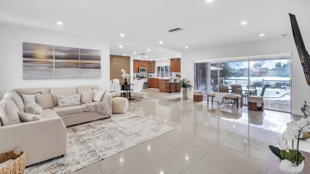 A spacious living area with a sofa, coffee table, and a view of the kitchen. - Lakefront Pool Family Home in Hollywood 10 minutes to HardRock stadium  (Pembroke Pines)