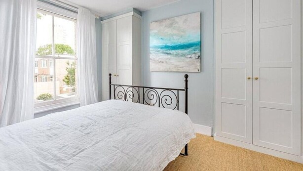 A bedroom with a bed, a window with curtains, a painting, and a wardrobe. - Herne Hill Haven (London)