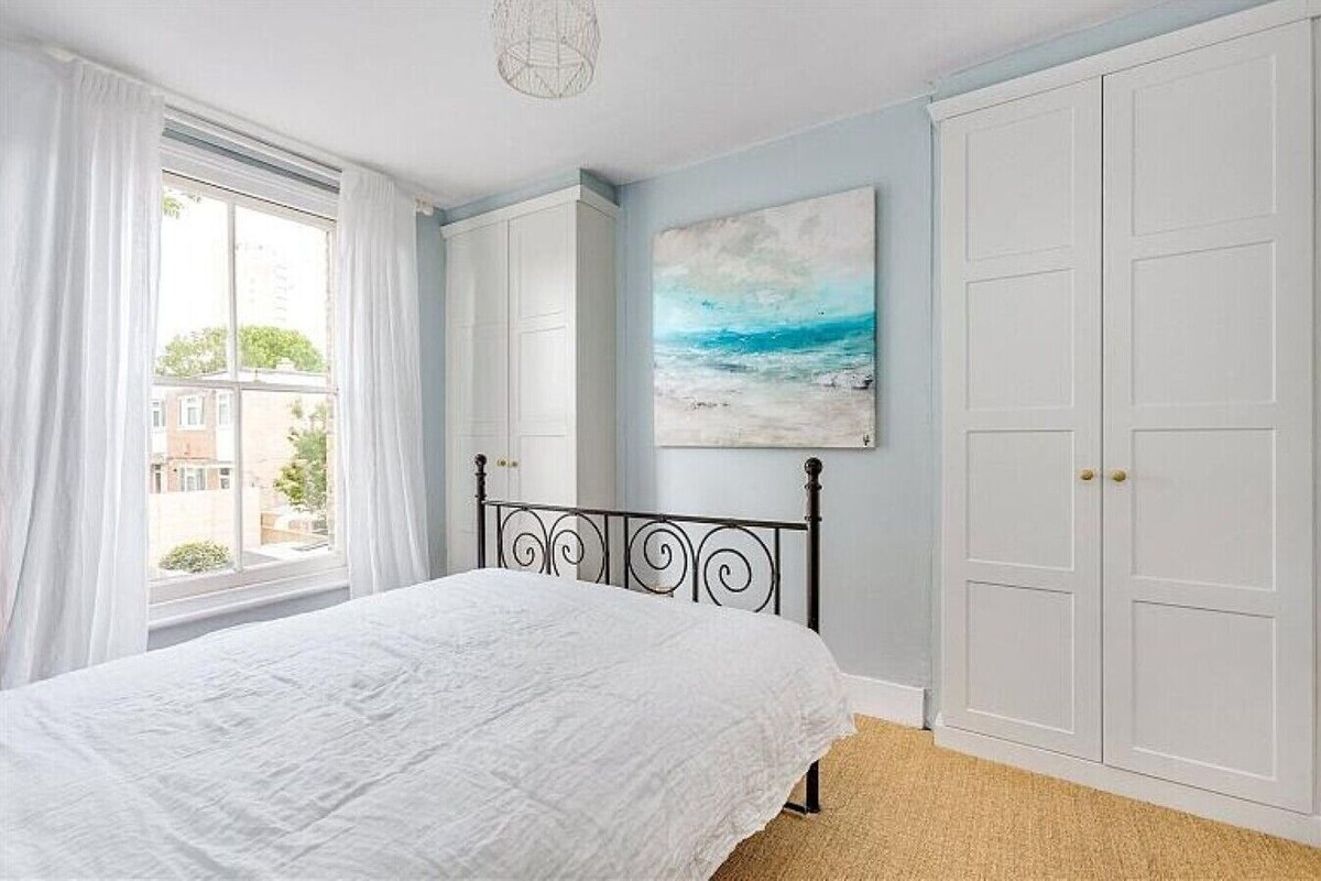 Ein Schlafzimmer mit einem Bett, einem Fenster mit Vorhängen, einem Gemälde und einem Kleiderschrank.