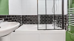 A bathroom with a white sink, a bathtub, and a glass-enclosed shower. - Herne Hill Haven (London)