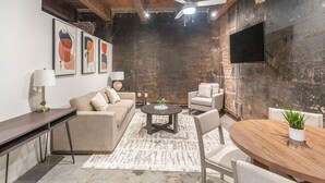 A modern living room with a sofa, chairs, a coffee table, and a dining table. There are abstract paintings on the wall and a TV mounted on the wall. -  Landing Furnished Apartments Downtown Memphis (Memphis)