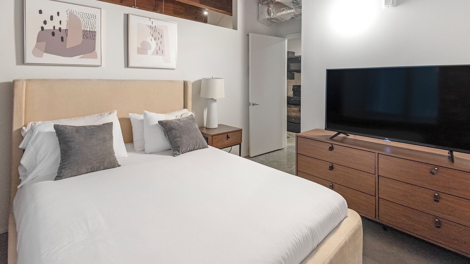 Une chambre à coucher moderne avec un grand lit, un téléviseur posé sur une commode en bois et des œuvres d’art accrochées au mur.