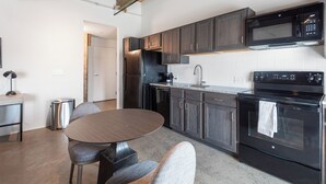 A modern kitchen with dark wood cabinets, a stainless steel refrigerator, a microwave, an oven, and a dining area with a round table and two chairs. -  Landing Furnished Apartments Downtown Memphis (Memphis)