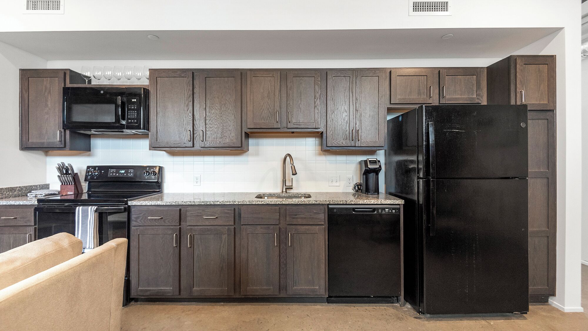 A modern kitchen with dark wood cabinets, a black refrigerator, a microwave, and a dishwasher.