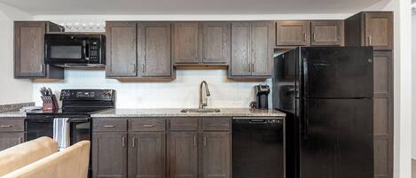 A modern kitchen with dark wood cabinets, a black refrigerator, a microwave, and a dishwasher.