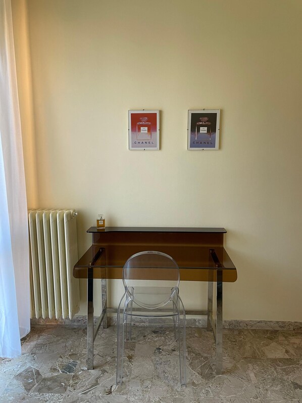 Een kamer met een bureau, stoel, radiator en twee ingekaderde posters aan de wand.