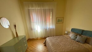 A bedroom with a bed, a bedside table, a mirror, a window with curtains, and a wall-mounted picture. - DA VINCI Residence - Between the Racetrack and the Historic Center (Imola)