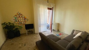 A living room with a sofa, a TV on a stand, a potted plant, and a colorful quilt on the wall. - DA VINCI Residence - Between the Racetrack and the Historic Center (Imola)