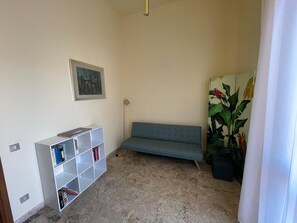 Een kamer met een blauwe bank, een witte boekenkast, een schilderij en een grote kamerplant.
