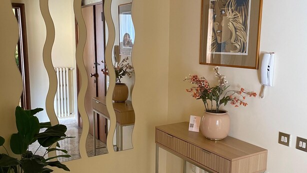 A room with a marble floor, a wooden console table with a vase of flowers, a framed artwork on the wall, and a decorative mirror with a wavy frame. - DA VINCI Residence - Between the Racetrack and the Historic Center (Imola)