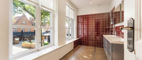 Un baño moderno con un ventanal grande, zona de ducha con azulejos rojos y un lavamanos blanco.