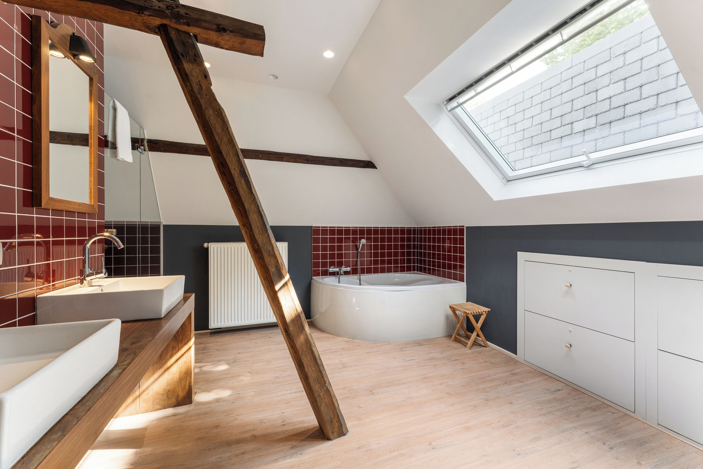 A modern bathroom with a skylight, a freestanding bathtub, and a wooden beam.