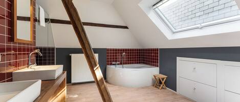 A modern bathroom with a skylight, a freestanding bathtub, and a wooden beam.