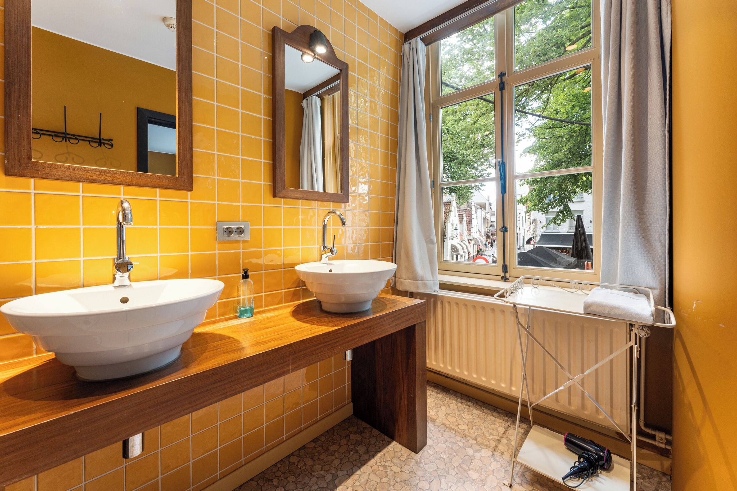 A bathroom with two sinks, a mirror, and a window with curtains.