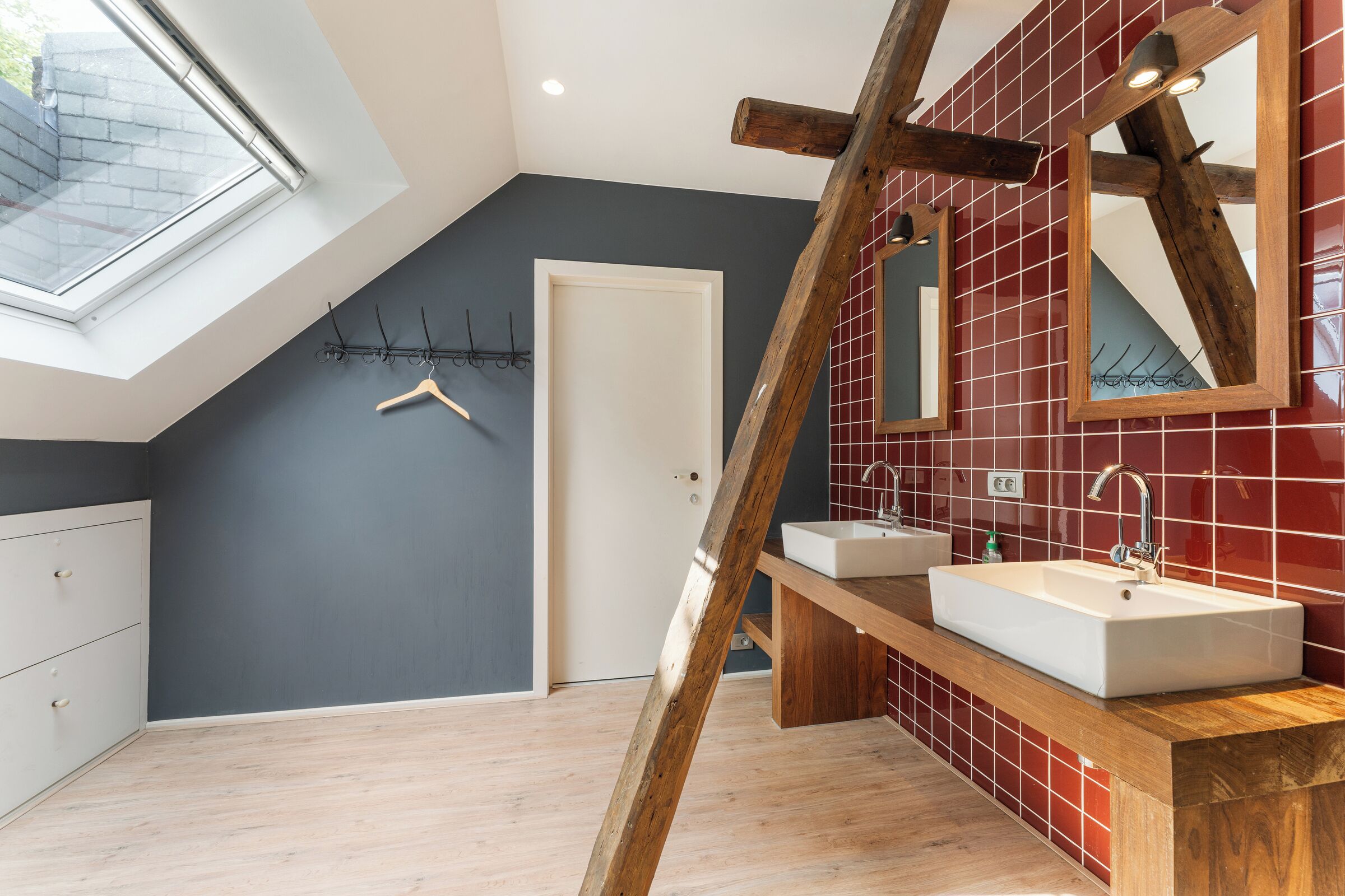 A modern bathroom with a skylight, two sinks, and a wooden beam structure.