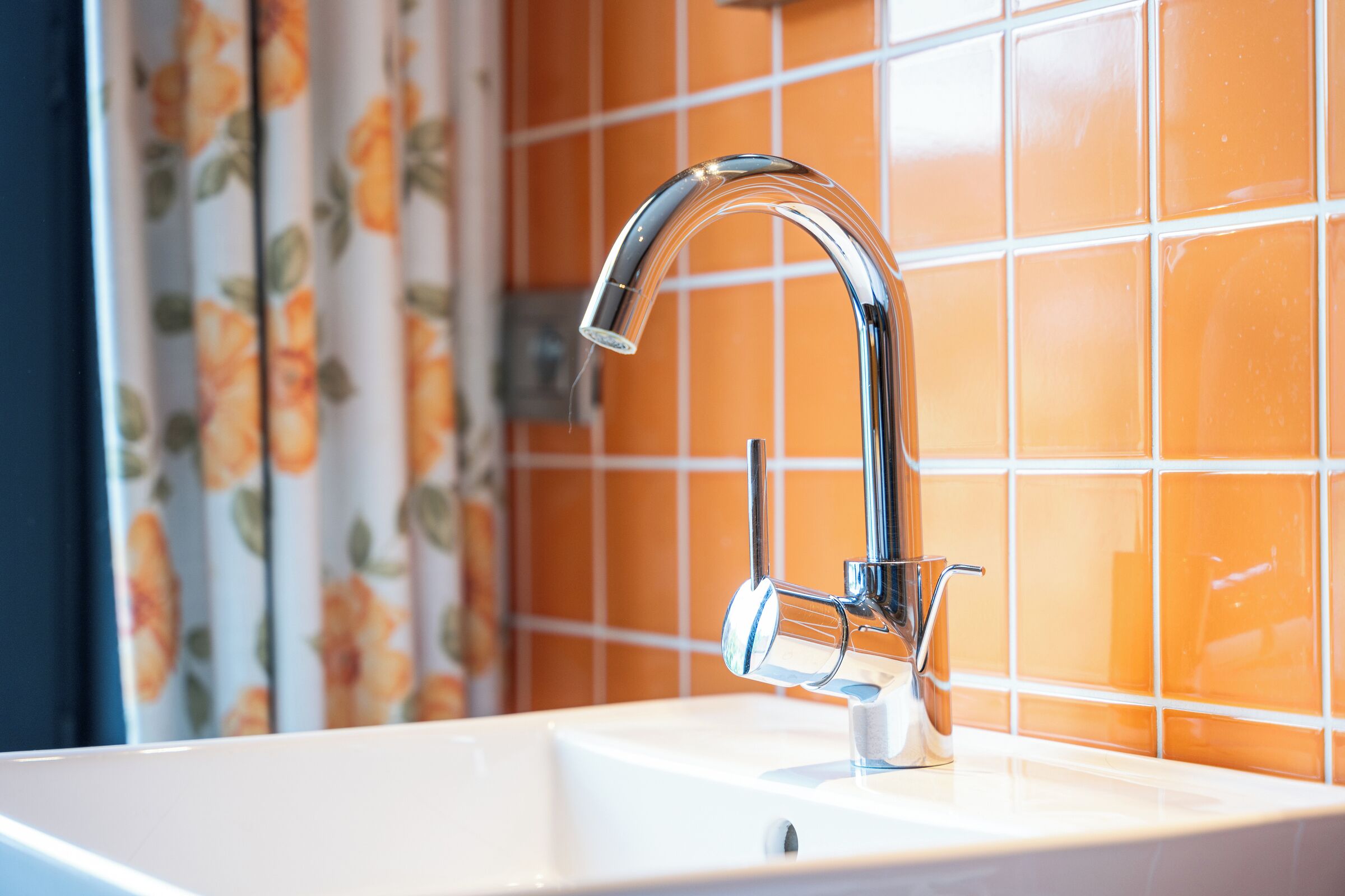 Ein Badezimmer mit einem chromfarbenen Wasserhahn, einem weißen Waschbecken und orangefarben gefliesten Wänden.