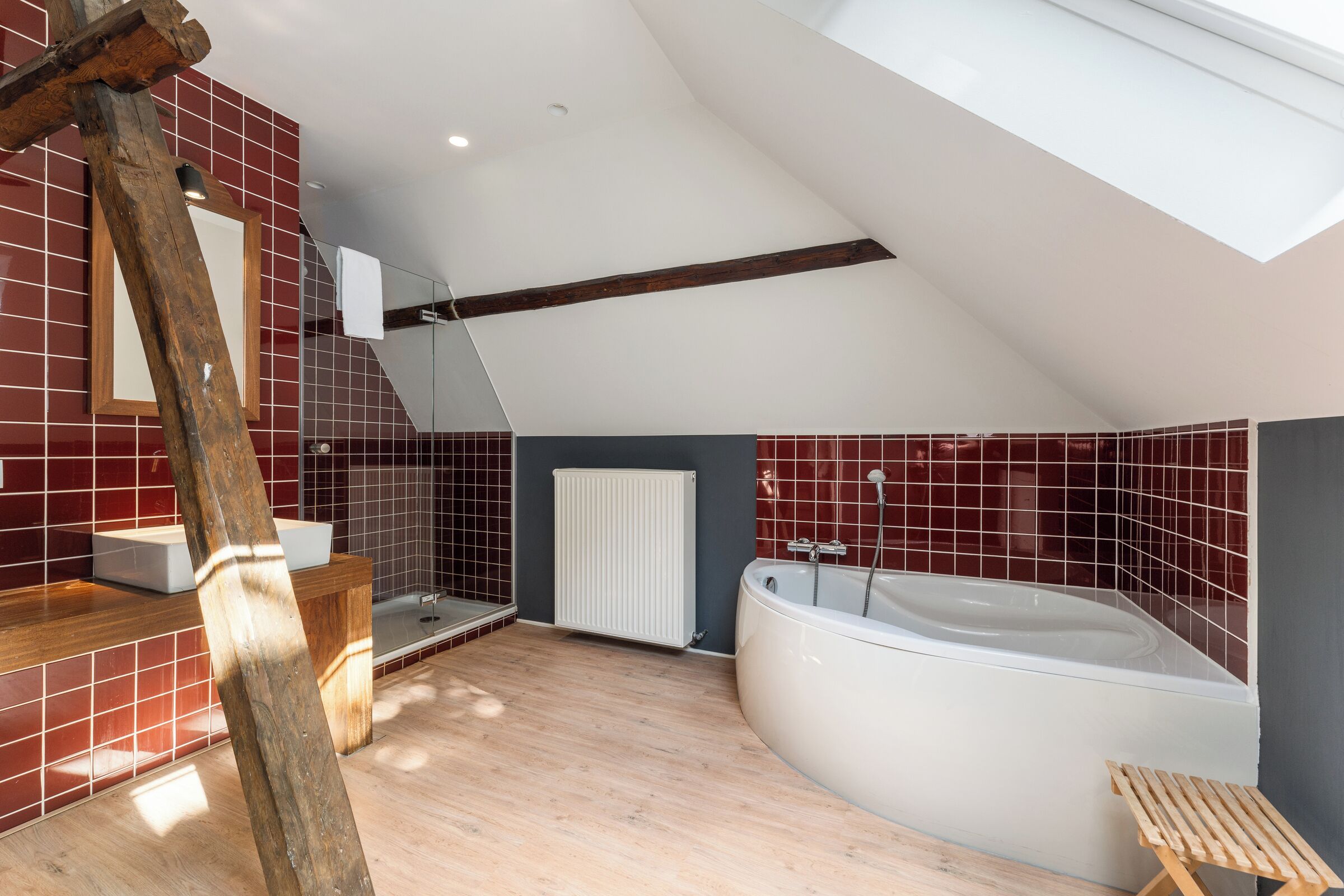 A modern bathroom with a freestanding bathtub, a wooden bench, and a large mirror.