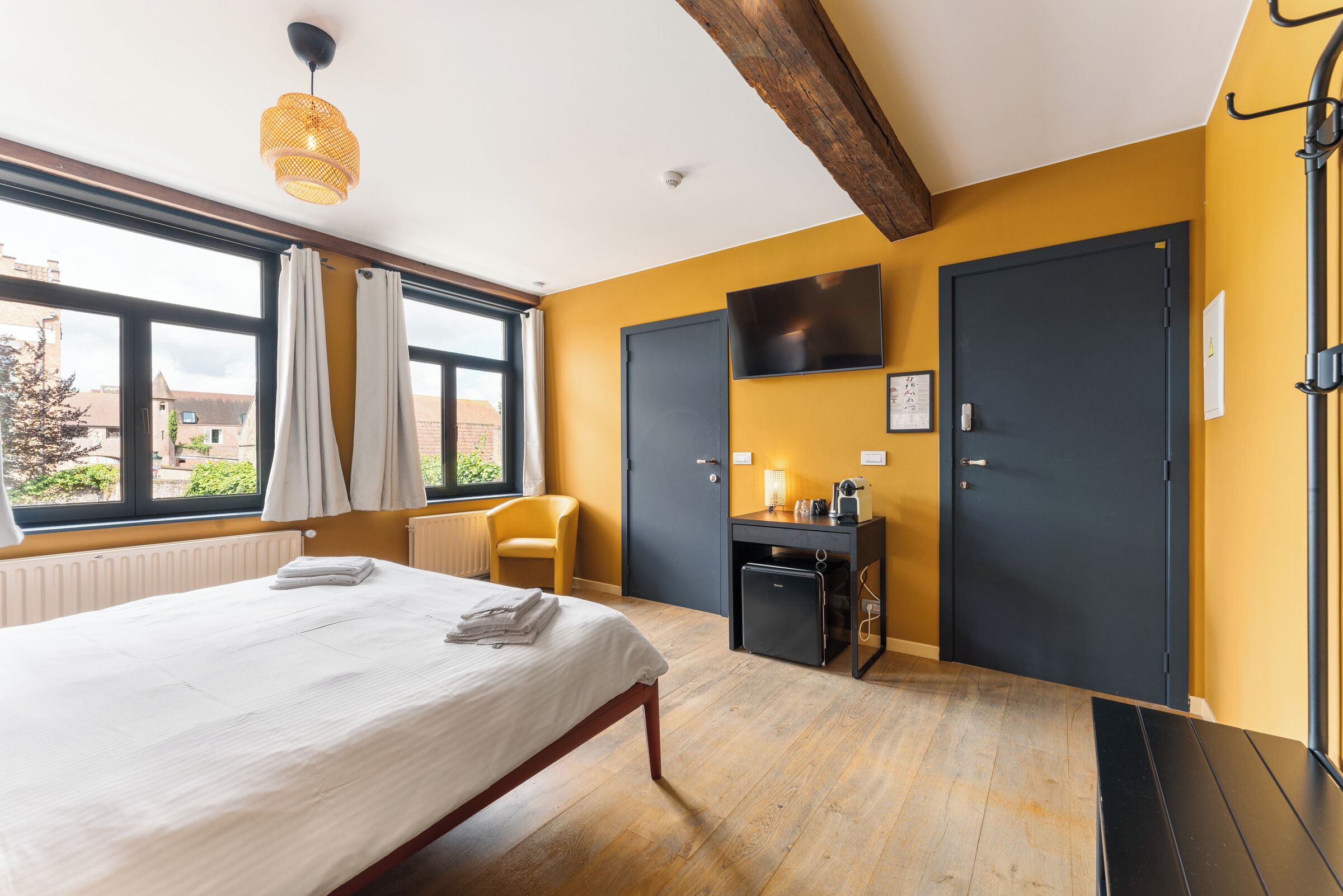 Une chambre d’hôtel avec un lit, un bureau, une chaise, une télévision et une fenêtre avec des rideaux.