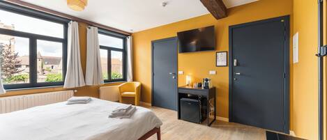 Une chambre d’hôtel avec un lit, un bureau, une chaise, une télévision et une fenêtre avec des rideaux.