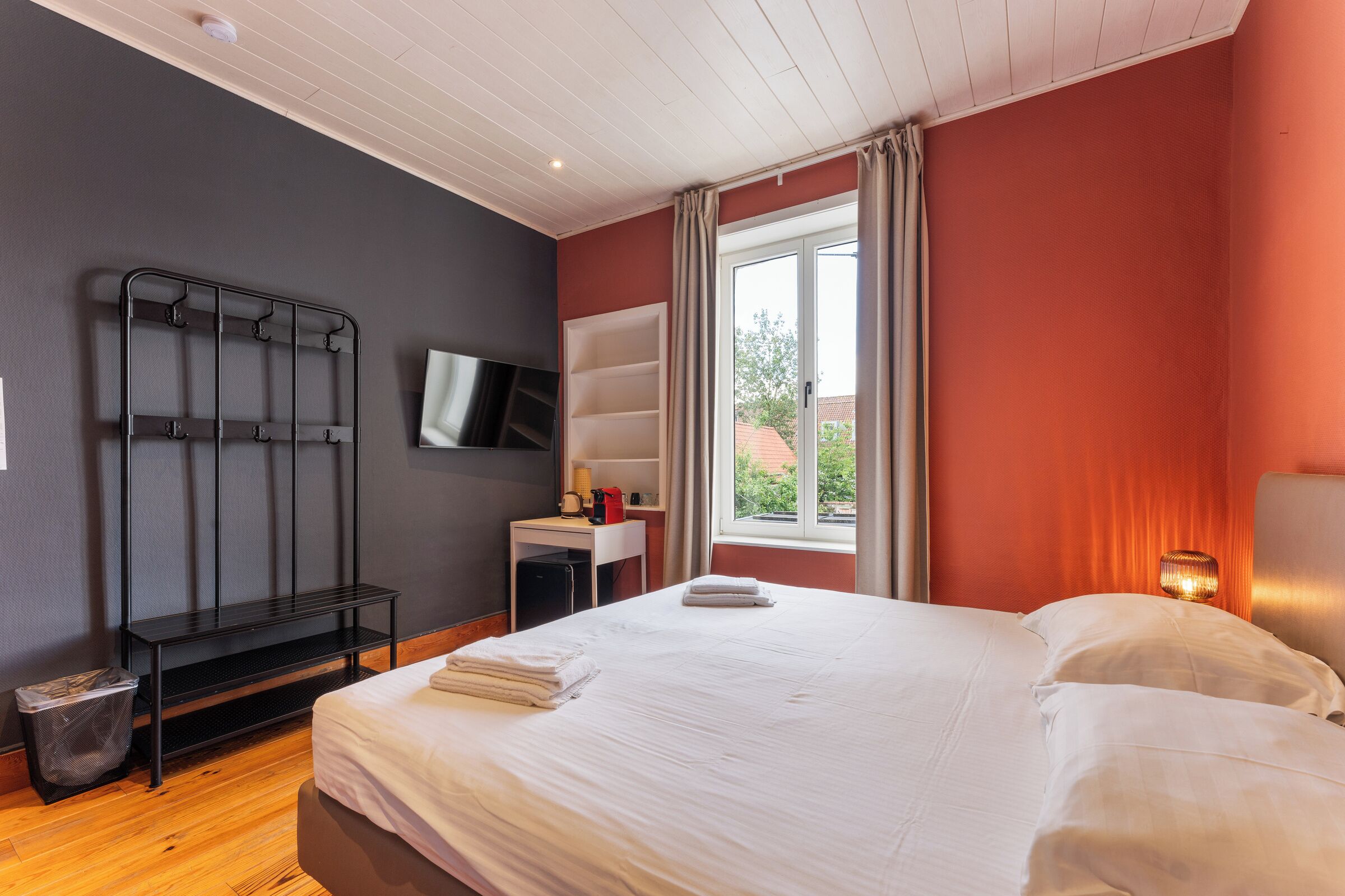 Hotelkamer met een bed, een bureau, een televisie, een raam met gordijnen en een wandplank.