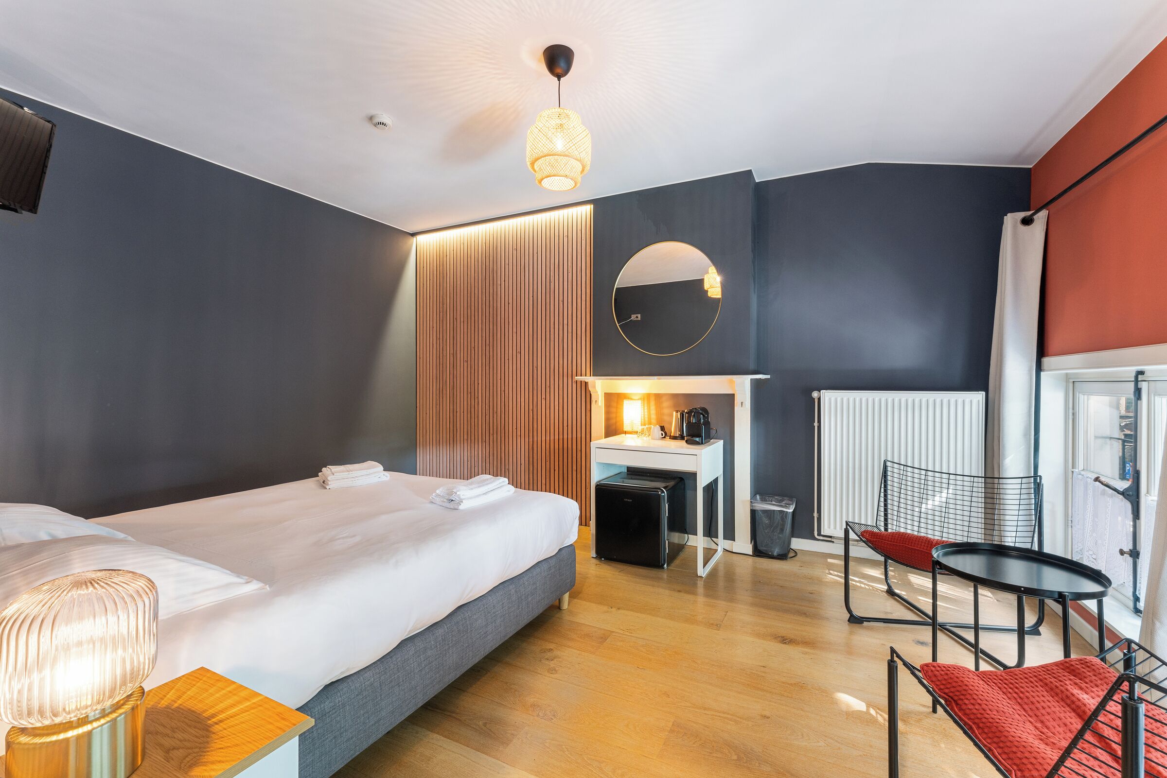 A modern hotel room with a large bed, a desk, a chair, and a small table.