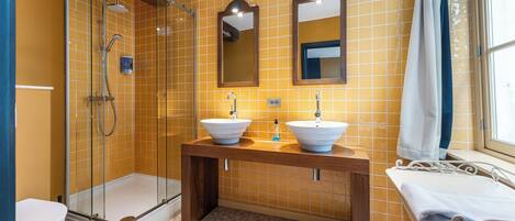 A bathroom with two sinks, a glass-enclosed shower, and a window with a curtain.