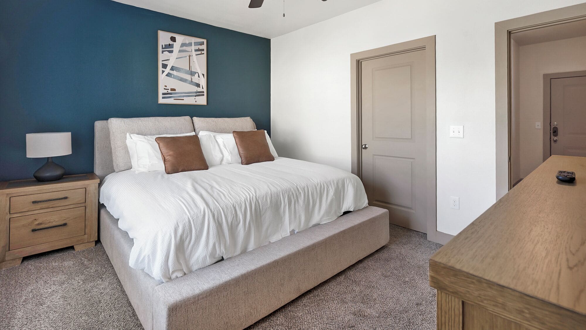Un dormitorio con cama, mesita de noche, escritorio y puerta.