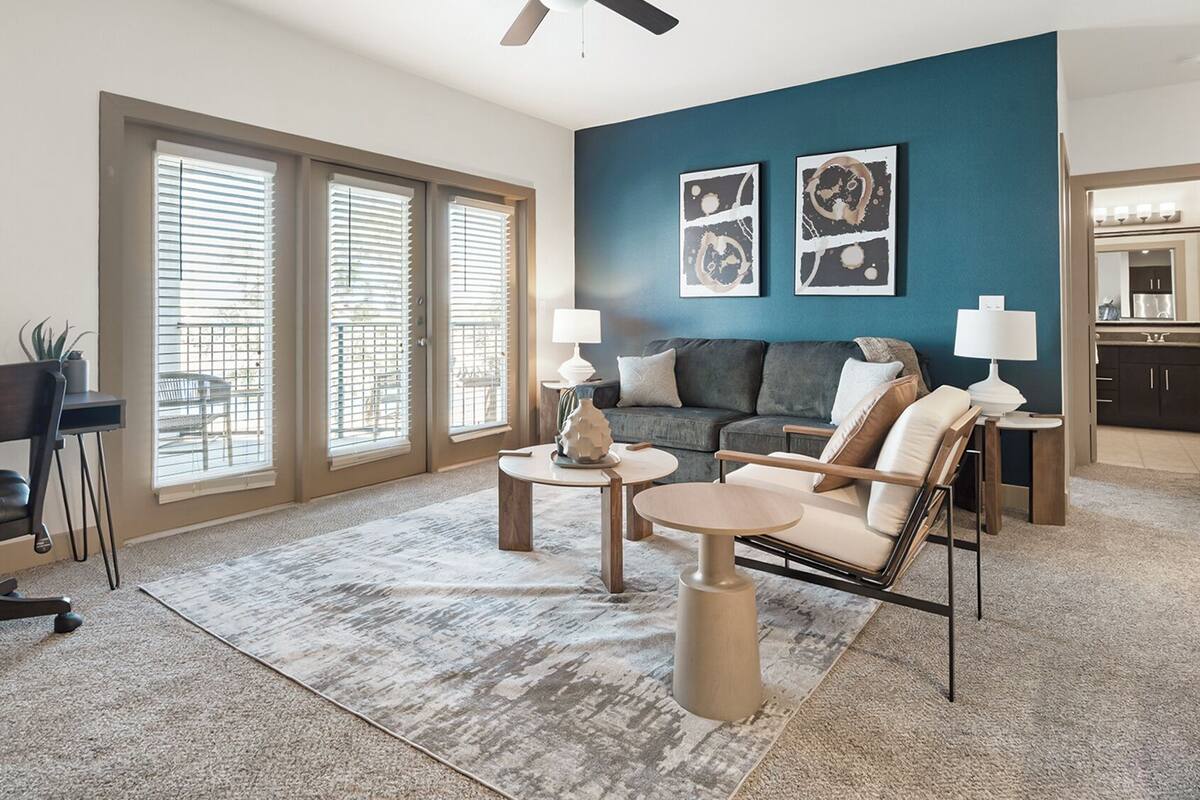 A spacious living room with a large window, a ceiling fan, and a view into the kitchen.