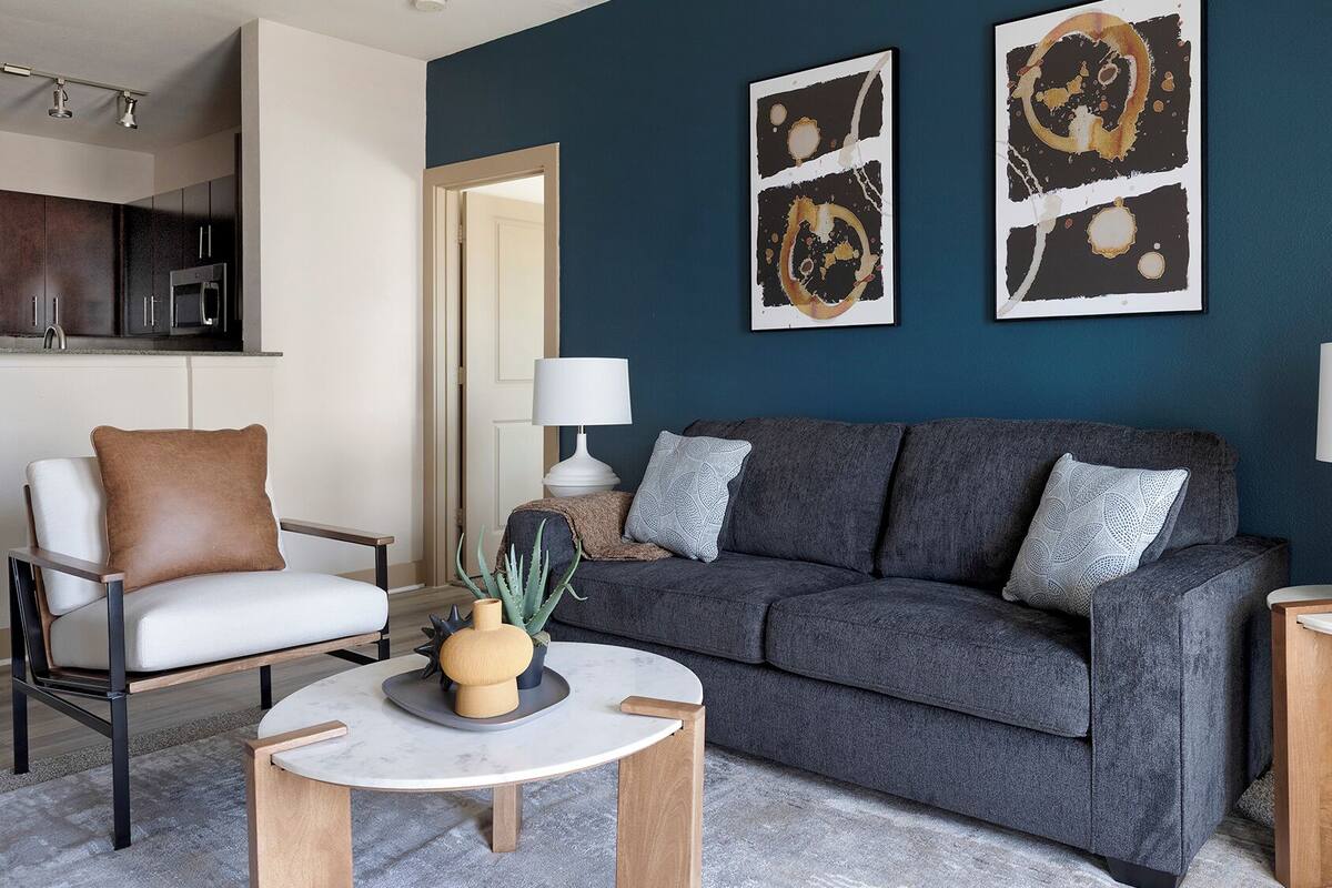 A modern living room with a grey sofa, a white armchair, and a coffee table. There are two wall-mounted lamps and a painting above the sofa.