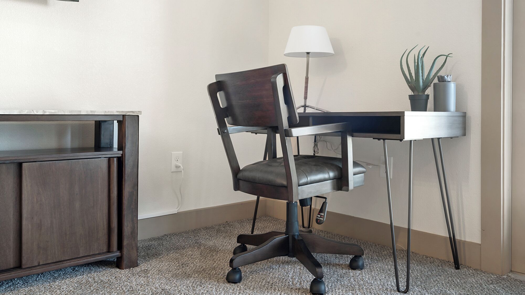 A modern office chair with wheels, a desk, a lamp, and a potted plant.