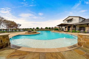 A swimming pool with a stone deck, a covered patio area, and a building in the background.