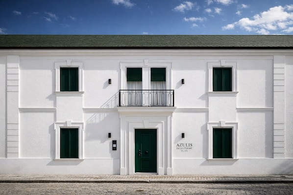 A white building with a green door, multiple windows, and a balcony.